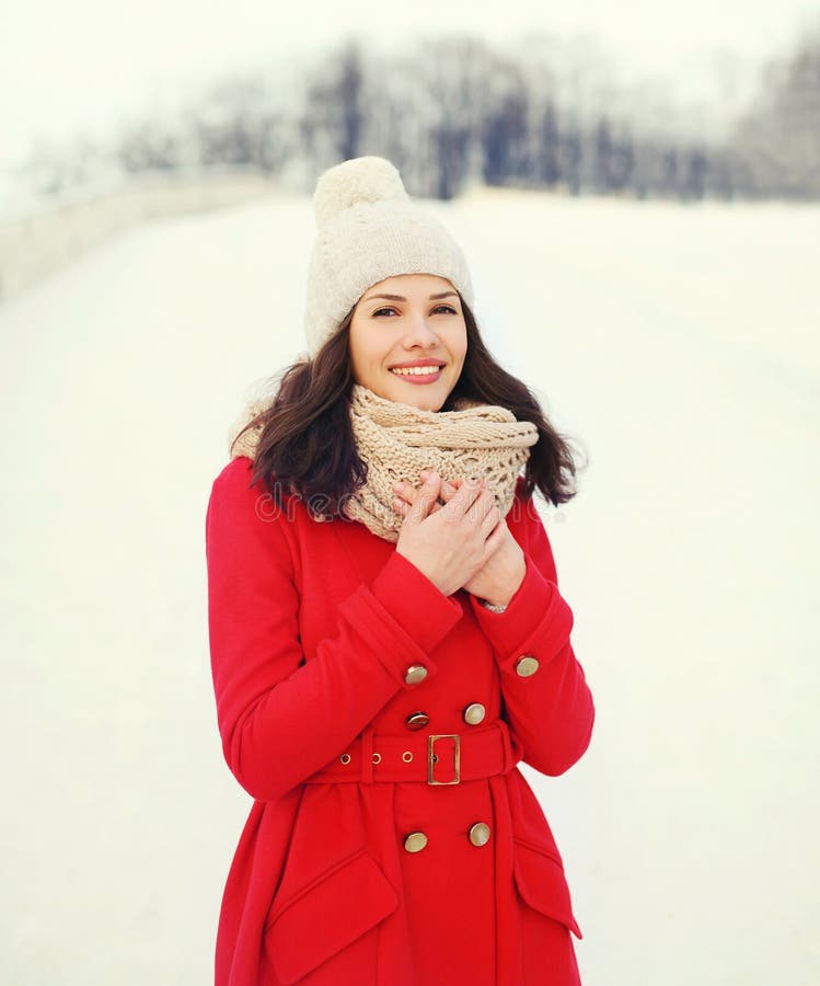 Mulher de sorriso nova feliz que veste um revestimento vermelho, um chapéu feito malha e um lenço no inverno fotografia de stock Mulher de sorriso nova feliz que veste um revestimento vermelho, um chapéu feito malha e um lenço no inverno fotografia de stock