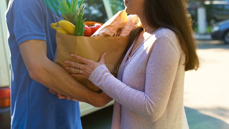 Mulher de sorriso que recebe o saco de mantimento do trabalhador da entrega, serviço do supermercado imagens de stock royalty free Mulher de sorriso que recebe o saco de mantimento do trabalhador da entrega, serviço do supermercado imagens de stock royalty free