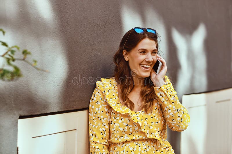 Mulher de sorriso que senta-se na cidade que fala em seu telefone celular imagens de stock royalty free Mulher de sorriso que senta-se na cidade que fala em seu telefone celular imagens de stock royalty free