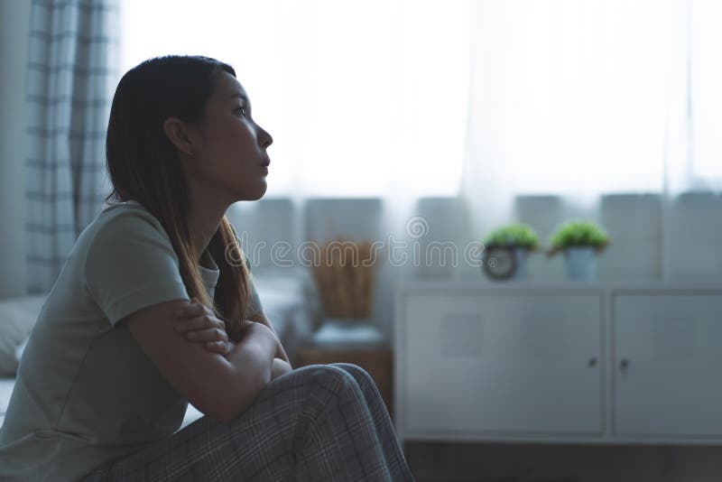 Uma mulher triste, sentada na beirada da cama, de noite. Conceito