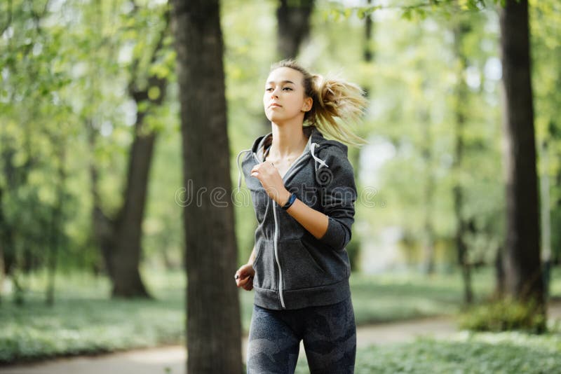 Mulher desportiva de sorriso dos jovens que corre no parque na manhã Menina da aptidão que movimenta-se no parque