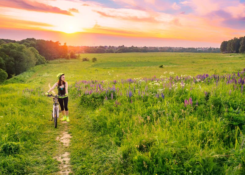 Mulher desportiva nova que monta uma bicicleta no por do sol A menina desportiva vai subida com bicicleta e aprecia o campo bonit imagem de stock royalty free Mulher desportiva nova que monta uma bicicleta no por do sol A menina desportiva vai subida com bicicleta e aprecia o campo bonit imagem de stock royalty free