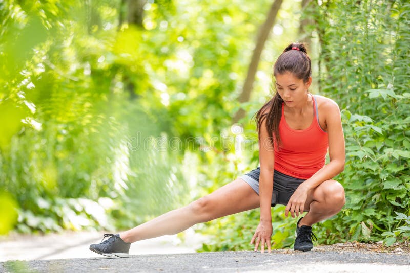 Mulher do corredor que estica a menina de corrida da corrida do exercício do pé que faz os estiramentos dos pés exteriores no par imagem de stock Mulher do corredor que estica a menina de corrida da corrida do exercício do pé que faz os estiramentos dos pés exteriores no par imagem de stock
