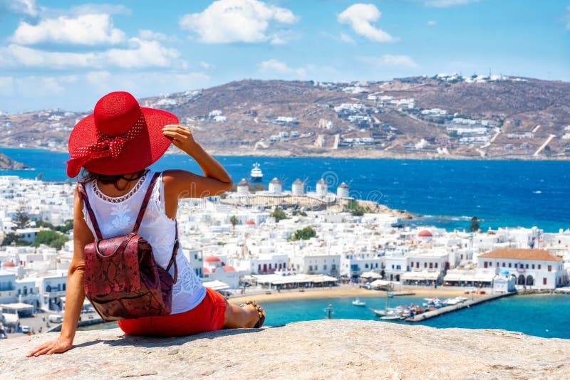 A mulher do viajante aprecia a vista em um monte sobre a cidade branca da ilha de Mykonos foto de stock A mulher do viajante aprecia a vista em um monte sobre a cidade branca da ilha de Mykonos foto de stock
