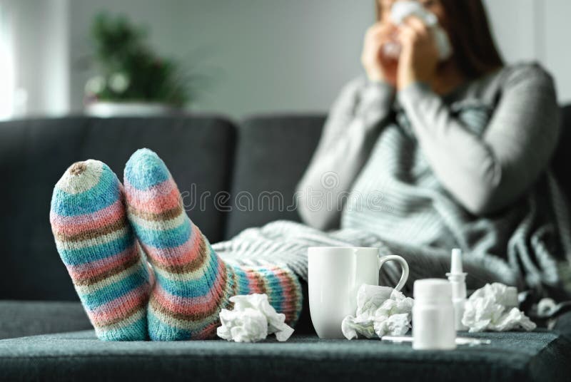 Mulher doente com a gripe, o frio, a febre e a tosse sentando-se no sofá em casa Nariz de sopro doente da pessoa e espirrar com t