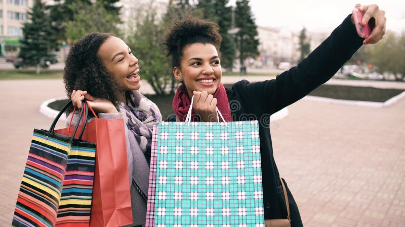 Mulher dois afro-americano bonito que toma o selfie com sacos de compras e sorriso Os amigos têm o divertimento após a venda de v imagens de stock Mulher dois afro-americano bonito que toma o selfie com sacos de compras e sorriso Os amigos têm o divertimento após a venda de v imagens de stock