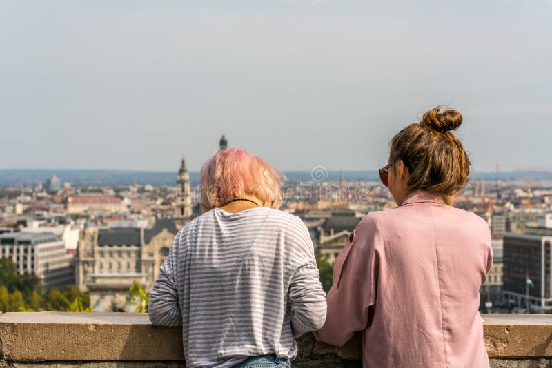 Mulher dois caucasiano nova que inclina-se sobre os trilhos de pedra para relaxar e olhar a opinião da cidade de Budapest Hungria foto de stock royalty free Mulher dois caucasiano nova que inclina-se sobre os trilhos de pedra para relaxar e olhar a opinião da cidade de Budapest Hungria foto de stock royalty free