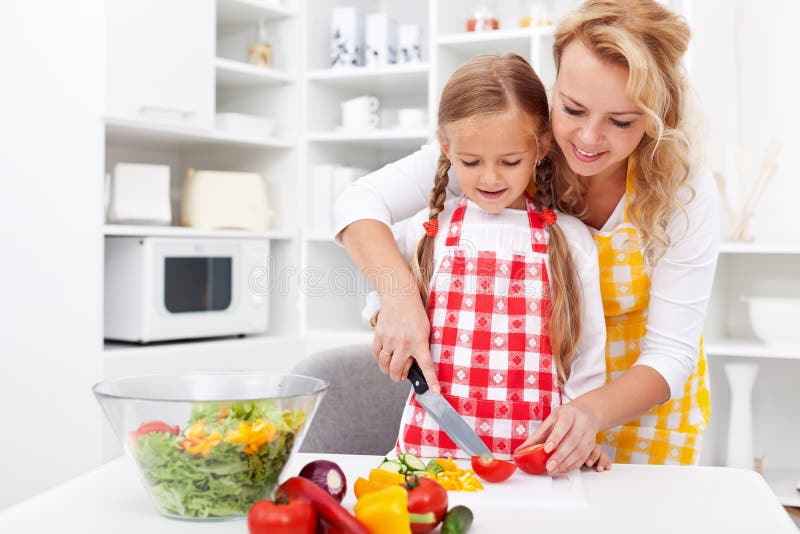 Mulher e menina a preparar uma salada de legumes fotografia de stock