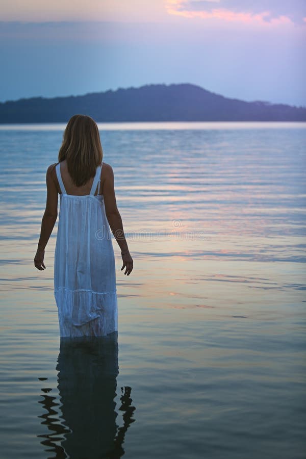 A mulher em águas do lago olha o por do sol roxo macio