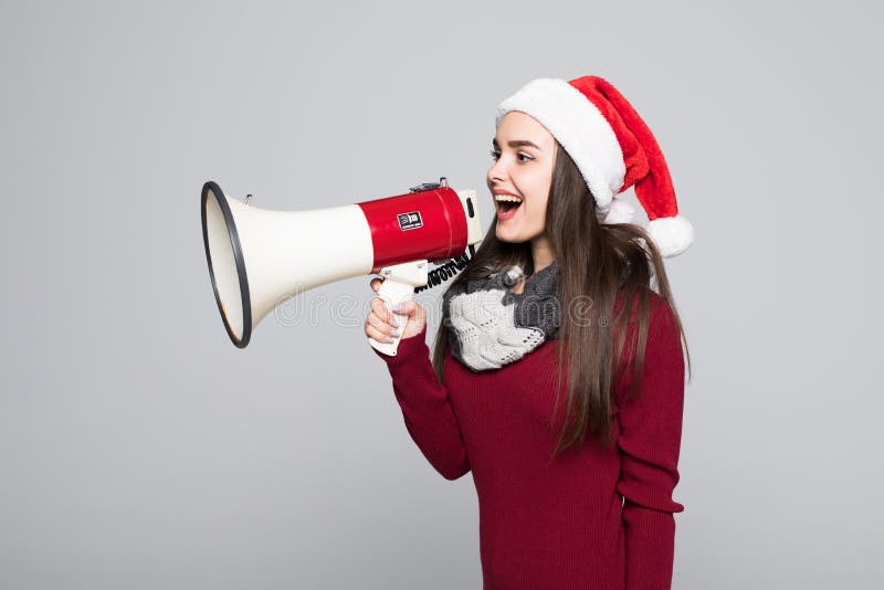 Mulher entusiasmado no chapéu de Santa que guarda o megafone sobre o fundo cinzento imagem de stock Mulher entusiasmado no chapéu de Santa que guarda o megafone sobre o fundo cinzento imagem de stock