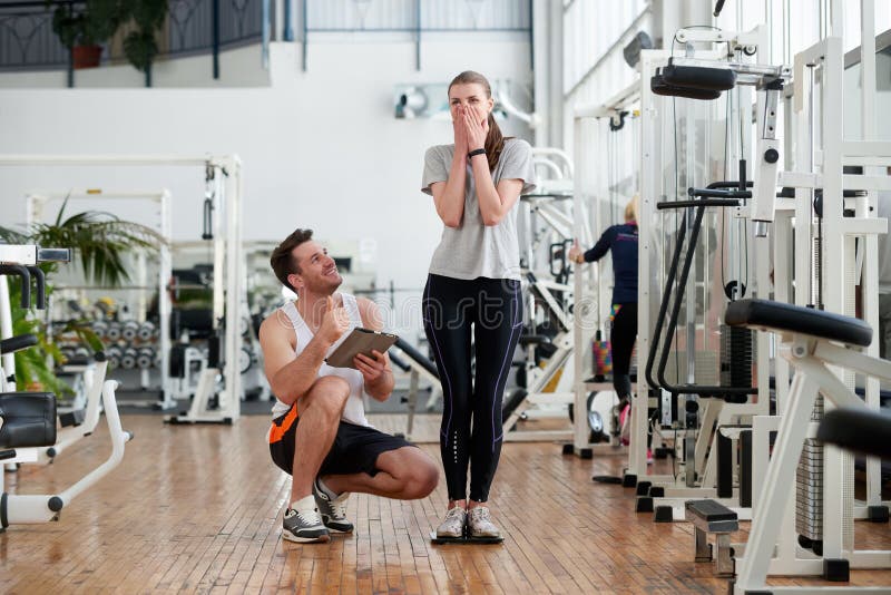 Mulher entusiasmado nova que pesa na escala no gym foto de stock Mulher entusiasmado nova que pesa na escala no gym foto de stock