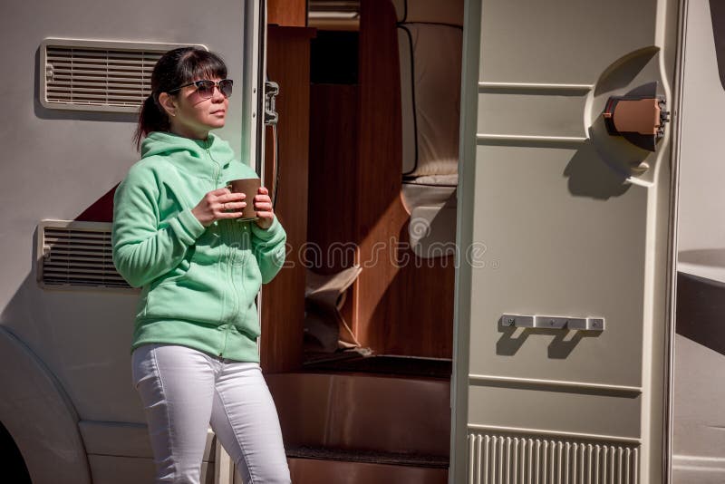 A mulher está estando com uma caneca de café perto do campista rv fotografia de stock royalty free A mulher está estando com uma caneca de café perto do campista rv fotografia de stock royalty free