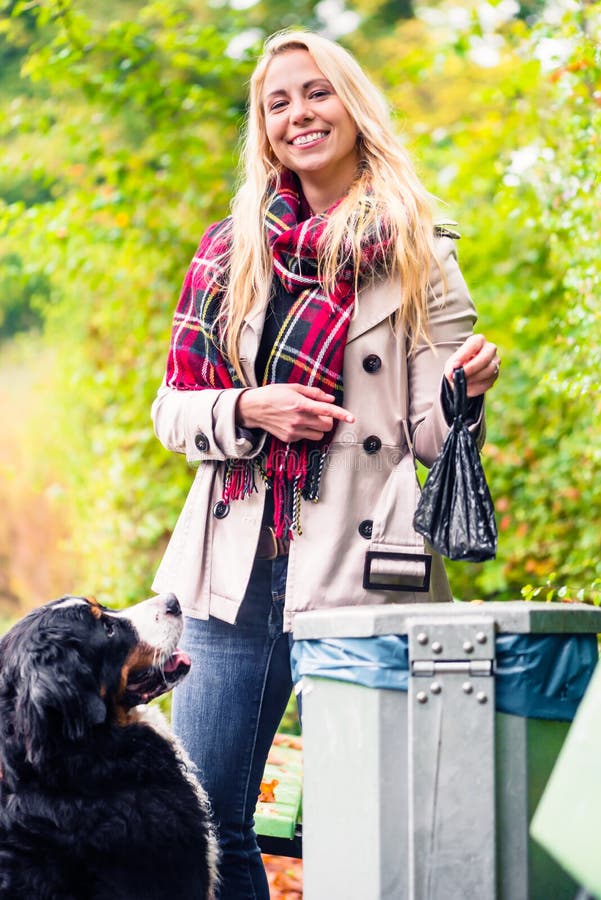 A mulher está pegarando o poo do cão que põe o no caixote de lixo fotografia de stock A mulher está pegarando o poo do cão que põe o no caixote de lixo fotografia de stock