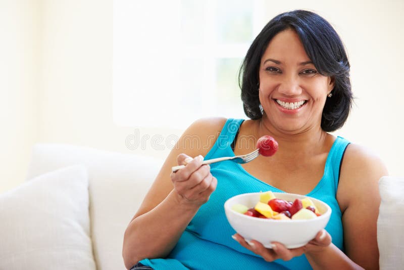Mulher excesso de peso que senta-se no fruto de Sofa Eating Bowl Of Fresh