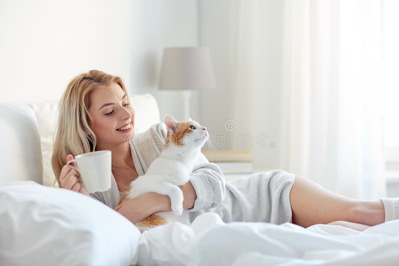 Mulher feliz com café e gato na cama em casa