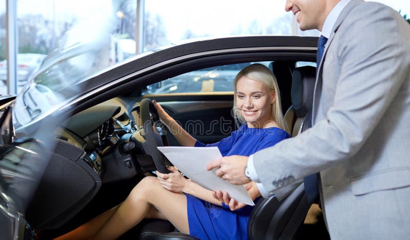 Auto business, car sale, consumerism and people concept - happy women with car dealer in auto show or salon. Auto business, car sale, consumerism and people concept - happy women with car dealer in auto show or salon