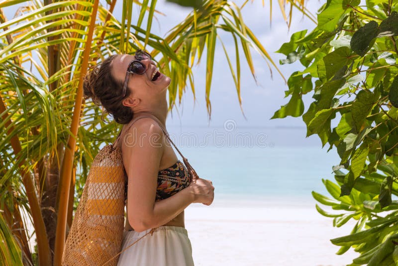 Mulher feliz nova com uma toalha que anda à praia em um destino tropical Riso ? c?mera imagens de stock royalty free Mulher feliz nova com uma toalha que anda à praia em um destino tropical Riso ? c?mera imagens de stock royalty free