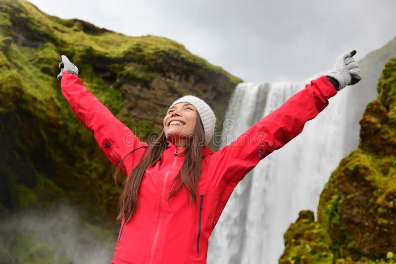 Happy woman by waterfall Skogafoss on Iceland posing serene and free outdoors. Girl visiting famous tourist attractions and landmarks in Icelandic nature landscape on Golden Circle. Happy woman by waterfall Skogafoss on Iceland posing serene and free outdoors. Girl visiting famous tourist attractions and landmarks in Icelandic nature landscape on Golden Circle.