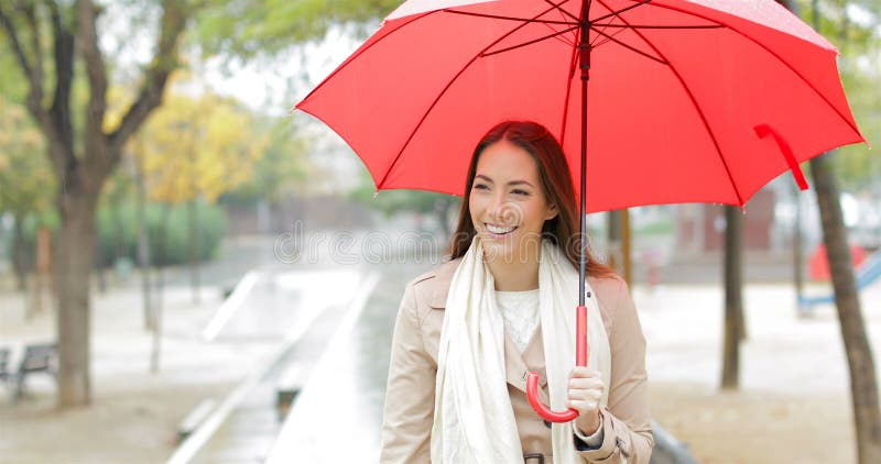 Mulher feliz que anda guardando um guarda-chuva sob a chuva