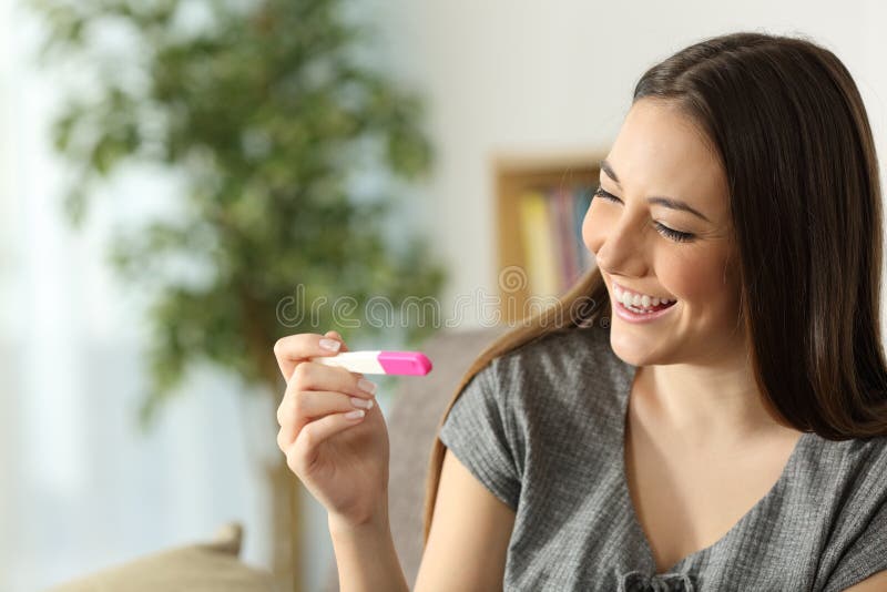 Happy woman checking pregnancy test sitting in a couch in the living room at home. Happy woman checking pregnancy test sitting in a couch in the living room at home