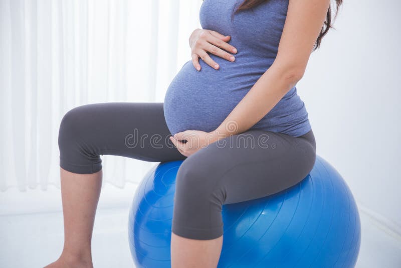 Mulher gravida asiática bonita que faz o exercício com uma bola suíça, imagem de stock royalty free Mulher gravida asiática bonita que faz o exercício com uma bola suíça, imagem de stock royalty free