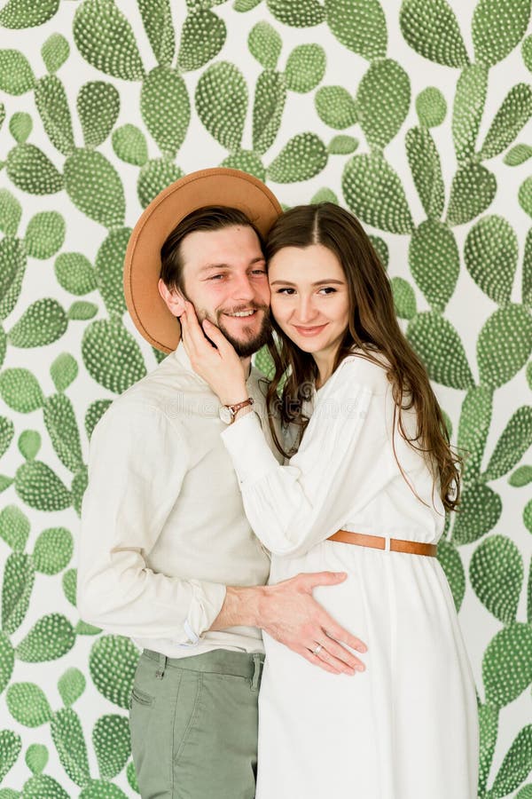 Mulher gravida bonita nova e seu marido na posição do chapéu perto da parede do cacto imagens de stock Mulher gravida bonita nova e seu marido na posição do chapéu perto da parede do cacto imagens de stock