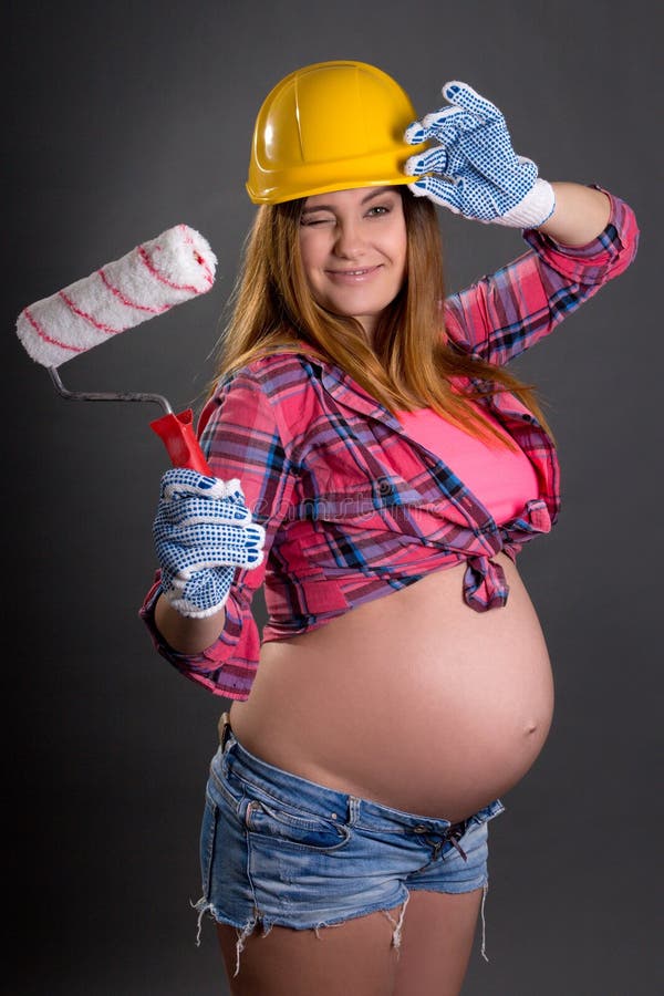 Mulher gravida bonita nova engraçada no capacete do construtor com p fotografia de stock royalty free Mulher gravida bonita nova engraçada no capacete do construtor com p fotografia de stock royalty free