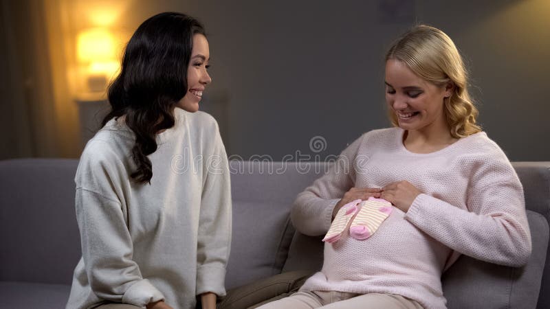 Mulher gravida feliz que guarda poucas peúgas em sua barriga, festa do bebê com amigo fotos de stock Mulher gravida feliz que guarda poucas peúgas em sua barriga, festa do bebê com amigo fotos de stock