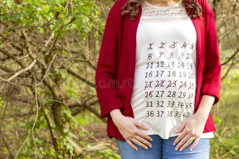 Mulher gravida no revestimento vermelho com o calendário em seu outdoo do t-shirt imagem de stock royalty free Mulher gravida no revestimento vermelho com o calendário em seu outdoo do t-shirt imagem de stock royalty free