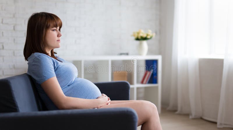 Mulher gravida pensativa que senta-se no sofá na sala de visitas fotografia de stock royalty free Mulher gravida pensativa que senta-se no sofá na sala de visitas fotografia de stock royalty free
