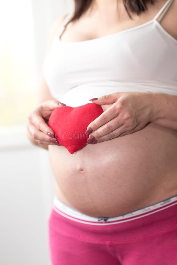 Mulher gravida que guarda um coração vermelho em sua barriga fotos de stock Mulher gravida que guarda um coração vermelho em sua barriga fotos de stock