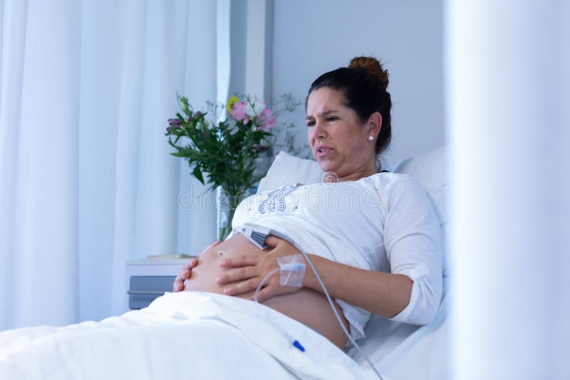 Mulher gravida que sofre da dor ao tocar em sua barriga na divisão foto de stock Mulher gravida que sofre da dor ao tocar em sua barriga na divisão foto de stock