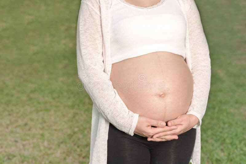 Mulher gravida que toca em sua barriga grande no jardim fotos de stock Mulher gravida que toca em sua barriga grande no jardim fotos de stock