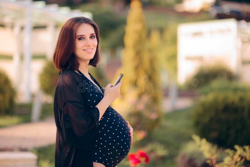 Mulher gravida que verifica seu telefone em férias da lua do bebê fotografia de stock Mulher gravida que verifica seu telefone em férias da lua do bebê fotografia de stock