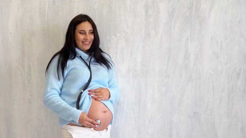 Mulher grávida bonita escuta com barriga de estetoscópio