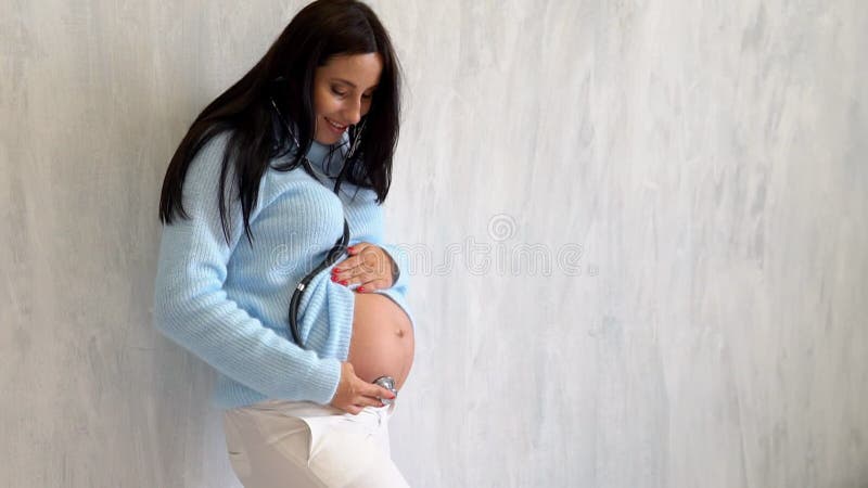 Mulher grávida bonita escuta com barriga de estetoscópio