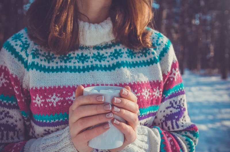 A mulher guarda a xícara de café com o marshmallow na floresta do inverno imagem de stock A mulher guarda a xícara de café com o marshmallow na floresta do inverno imagem de stock