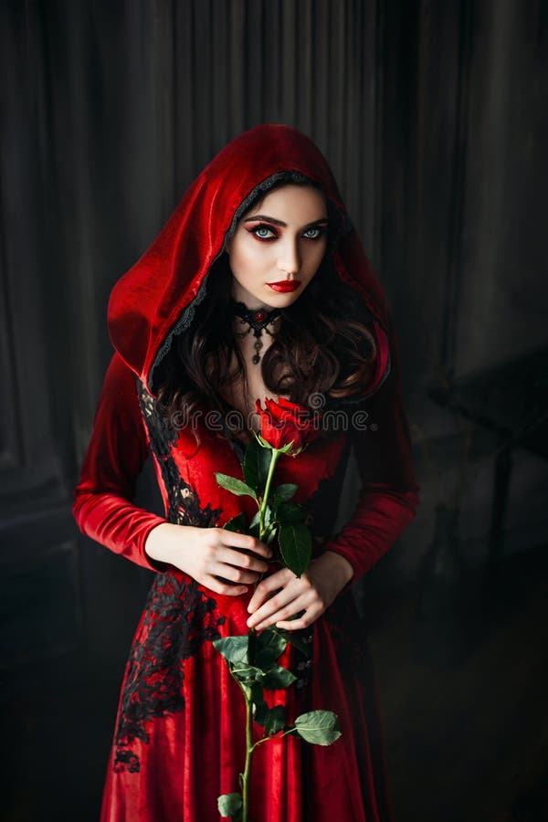 Mulher gótica. capuz de roupas velvet. cabelo ondulado. colar preto. rosa nas mãos foto de stock