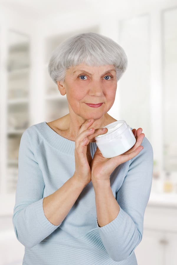 Mulher idosa encantador que aplica o creme cosmético em sua cara para cuidados com a pele faciais no banheiro em casa foto de stock royalty free Mulher idosa encantador que aplica o creme cosmético em sua cara para cuidados com a pele faciais no banheiro em casa foto de stock royalty free