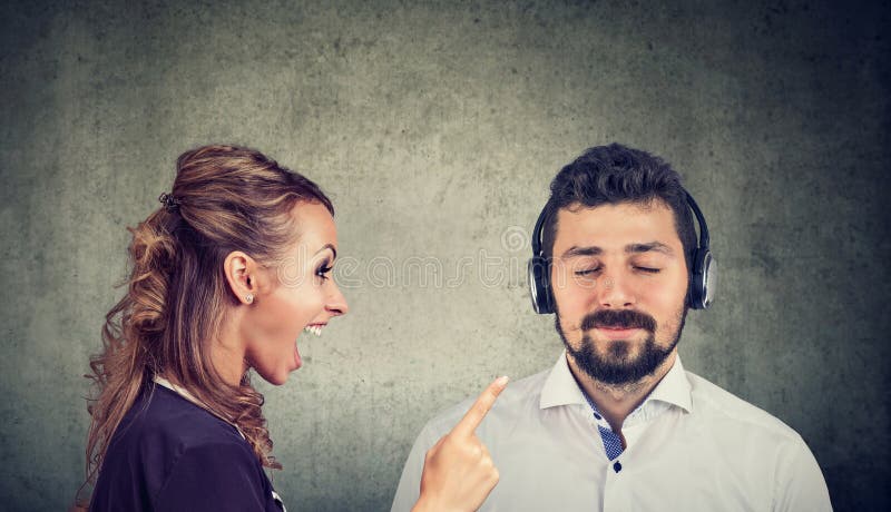 Mulher irritada que grita em um marido calmo que escuta a música foto de stock Mulher irritada que grita em um marido calmo que escuta a música foto de stock