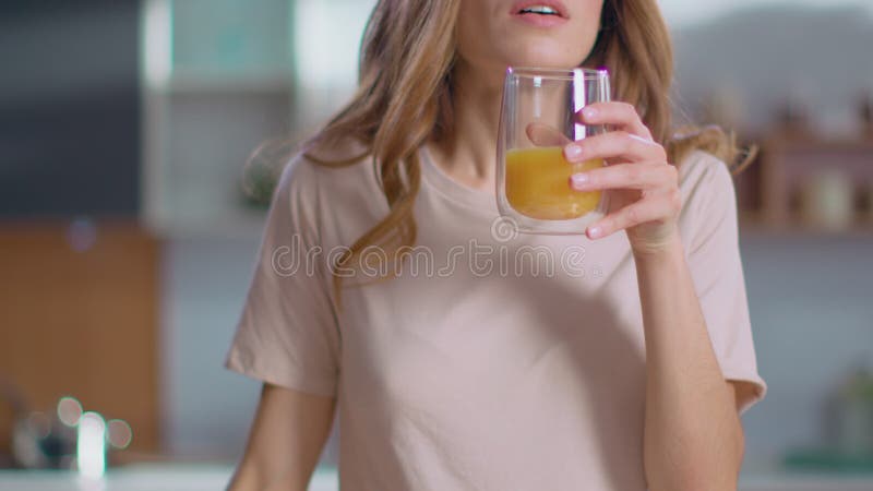 Mulher jogando suco no copo da cozinha. senhora tomando suco de laranja