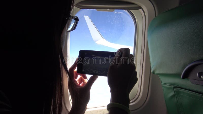 mulher 4K asiática que usa o telefone esperto pela janela um avião