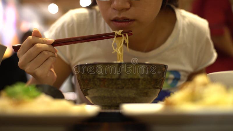 mulher 4K asiática que usa varas para comer o macarronete da carne, alimento chinês do restaurante