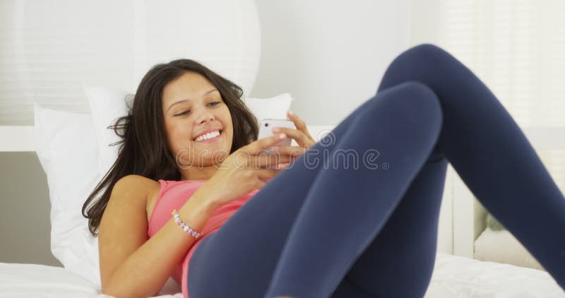 Mulher latino-americano nova que encontra-se na cama que texting e que ri imagens de stock royalty free Mulher latino-americano nova que encontra-se na cama que texting e que ri imagens de stock royalty free