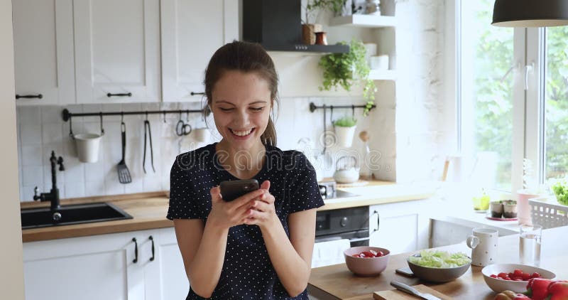 Mulher lendo ótimas notícias se sente animada enquanto fica na cozinha