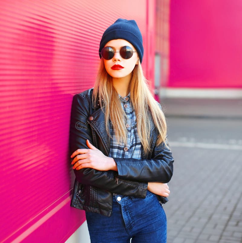 Mulher loura nova do retrato à moda no revestimento do estilo do preto da rocha, chapéu que levanta na rua da cidade sobre a pare fotografia de stock Mulher loura nova do retrato à moda no revestimento do estilo do preto da rocha, chapéu que levanta na rua da cidade sobre a pare fotografia de stock