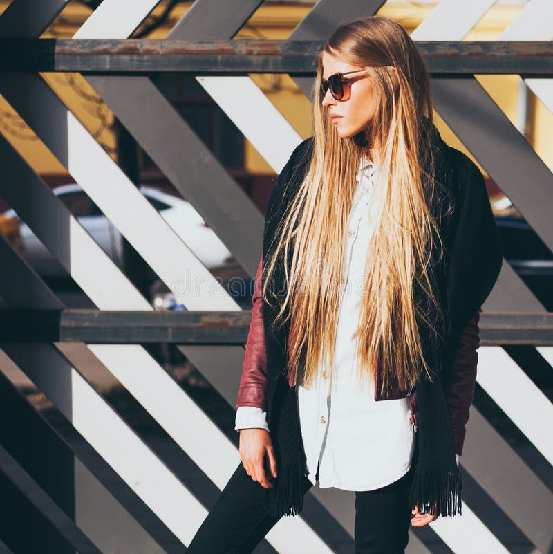 Mulher loura nova nos óculos de sol e um equipamento elegante que levanta na noite morna da mola da rua Blogger da forma fotografia de stock royalty free Mulher loura nova nos óculos de sol e um equipamento elegante que levanta na noite morna da mola da rua Blogger da forma fotografia de stock royalty free