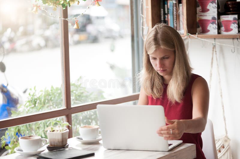 Mulher loura nova que datilografa no portátil no café imagens de stock royalty free Mulher loura nova que datilografa no portátil no café imagens de stock royalty free