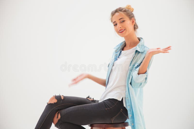 Mulher loura ocasional que senta-se na cadeira e nas boas vindas você fotos de stock Mulher loura ocasional que senta-se na cadeira e nas boas vindas você fotos de stock