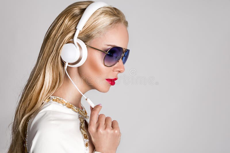 Mulher loura 'sexy' bonita com cabelo longo e corpo perfeito em um terno branco elegante que senta-se com fones de ouvido imagens de stock royalty free Mulher loura 'sexy' bonita com cabelo longo e corpo perfeito em um terno branco elegante que senta-se com fones de ouvido imagens de stock royalty free